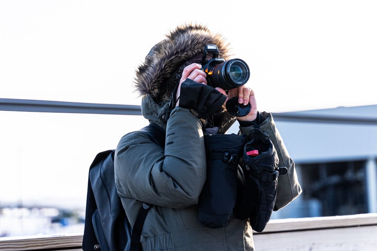 A photographer wearing a winter parka capturing outdoor scenes with a camera.