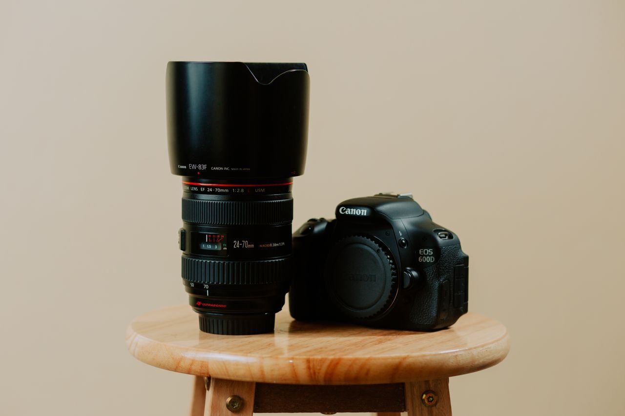 Close-up of a DSLR camera and lens displayed on a wooden stool, against a neutral background.