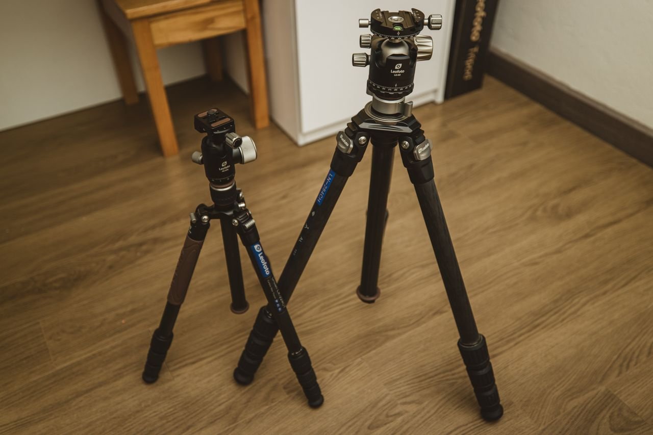 Two professional tripods standing on a wooden floor indoors, ideal for photography enthusiasts.