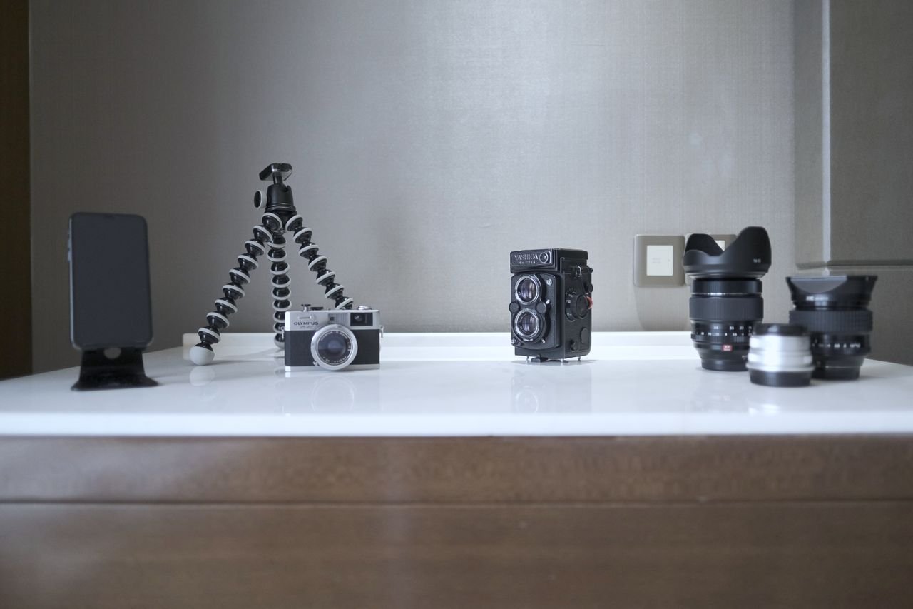 A collection of vintage and modern photography equipment, including cameras and lenses, creatively arranged on a table.